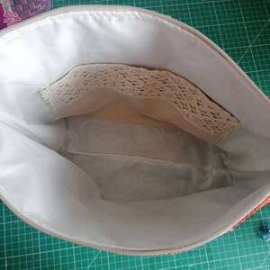 May include: The inside of a red and white zippered pouch with a white lining. The pouch has a small pocket with a lace trim.