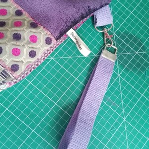May include: A purple and green fabric bag with a purple strap and a silver clasp. The bag has a label that says "SuzieQmakes".