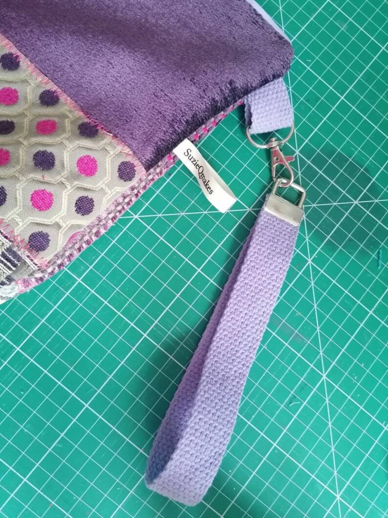 May include: A purple and green fabric bag with a purple strap and a silver clasp. The bag has a label that says "SuzieQmakes".