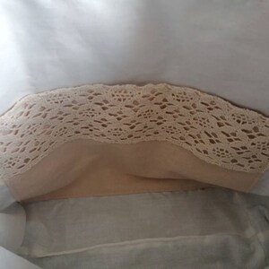 May include: A white fabric bag with a beige lace trim. The bag is open and the inside is lined with a beige fabric.