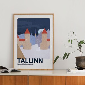 May include: A framed art print depicting Tallinn's city walls at night. The illustration shows beige towers with red roofs, a full moon, and the city name in bold text. The print is displayed on a white surface, with a wooden frame.
