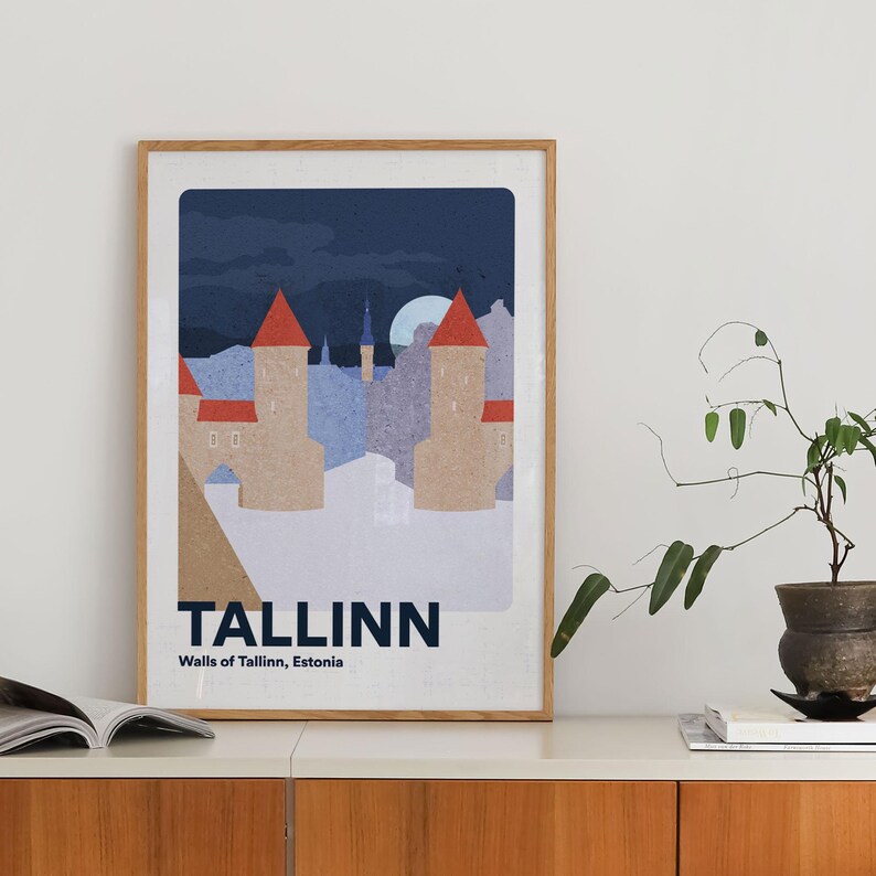 May include: A framed art print depicting Tallinn's city walls at night. The illustration shows beige towers with red roofs, a full moon, and the city name in bold text. The print is displayed on a white surface, with a wooden frame.