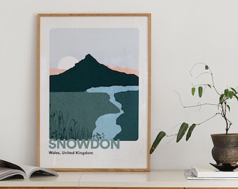 May include: A framed art print featuring a landscape illustration of Snowdon in Wales, United Kingdom. The artwork depicts a mountain, river, and sunset in shades of green, blue, and pink. The word "SNOWDON" is printed at the bottom.