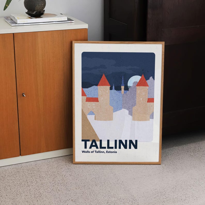 May include: A framed art print depicting Tallinn, Estonia, with a stylized illustration of the city's walls and towers under a dark blue sky and a full moon. The print is in a wooden frame and includes the word "TALLINN".