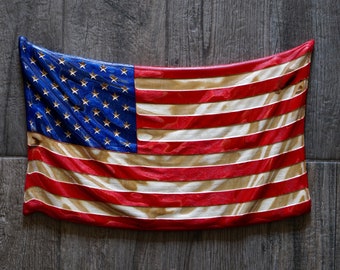 May include: A wooden carving of the American flag, painted in red, white, and blue. The flag is hanging on a gray wood background.