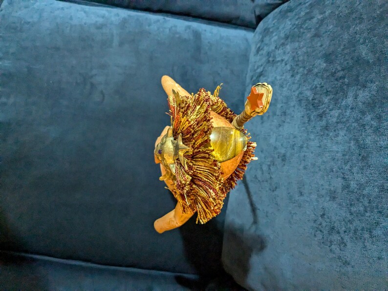 May include: A gold-colored decorative object with a lion's head and a red star on top. The object is made of metal and has a fringe of gold tassels.