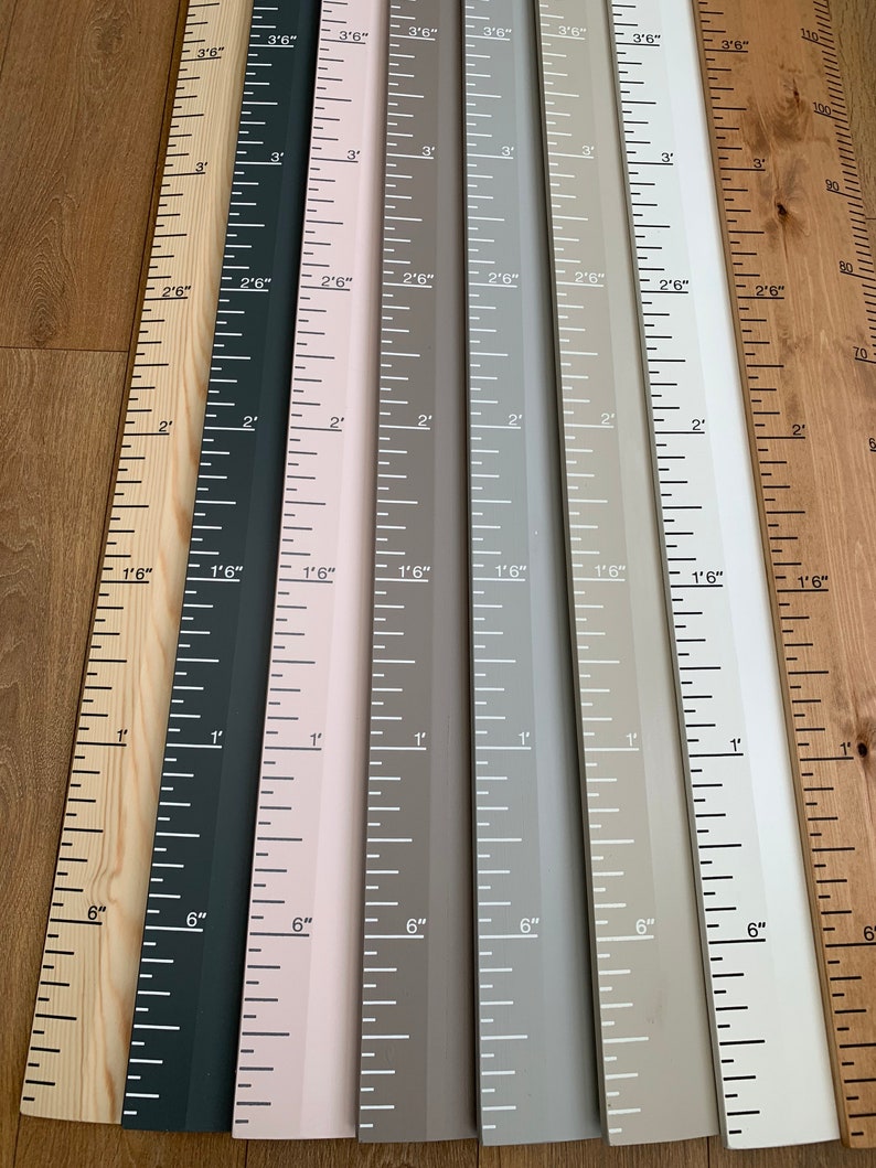May include: A collection of wooden height charts in various colors, including natural wood, black, pink, gray, and white. Each chart is marked with inch and foot measurements, ideal for tracking growth. The charts are arranged side by side.