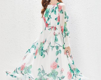 Puede incluir: Un vestido maxi blanco con estampado floral de rosas rosas y hojas verdes. El vestido tiene mangas largas y un lazo en la cintura.