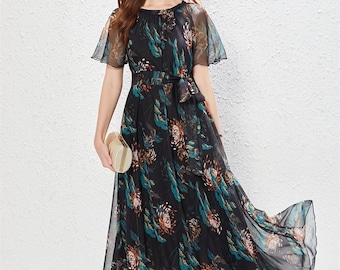 Puede incluir: Un vestido maxi negro con estampado floral en tonos verdes y marrones. El vestido tiene un escote redondo, mangas cortas y un lazo en la cintura.