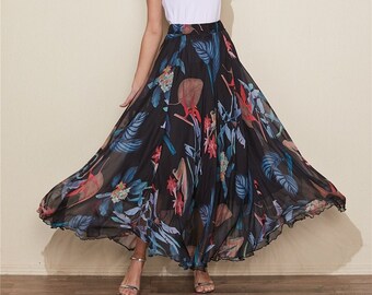 May include: A woman wearing a white t-shirt and a long, flowing black skirt with a colorful floral print. The skirt has a high waist and a ruffled hem.