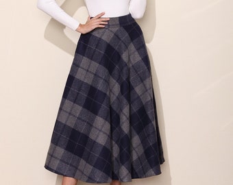 May include: A woman wearing a white long-sleeved shirt and a navy blue and gray plaid midi skirt. She is wearing black high heels.