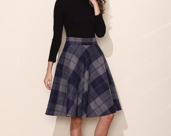 May include: A woman wearing a black mock neck shirt and a blue and gray plaid skirt. She is wearing black heels.