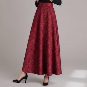 Op de afbeelding: Een lange, vloeiende rode rok met een subtiel zwart patroon. De rok wordt gecombineerd met een zwarte coltrui en zwarte hakken. De outfit is geschikt voor formele of semi-formele gelegenheden.