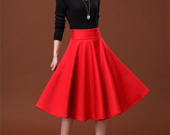 May include: A woman wearing a black long-sleeved sweater and a red high-waisted skirt. The skirt is a-line and falls to just above her knees. She is wearing black high heels.