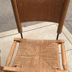 May include: A wooden bar stool with a woven cane seat and back. The stool has a dark brown finish and a black metal frame.