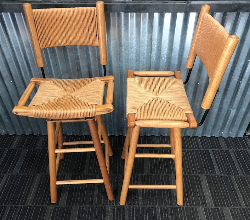 May include: Two wooden bar stools with woven cane seats and backs. The stools have a black metal frame and are made of natural wood.