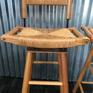 May include: A wooden bar stool with a woven cane seat and back. The stool has a simple design with four legs and a footrest.