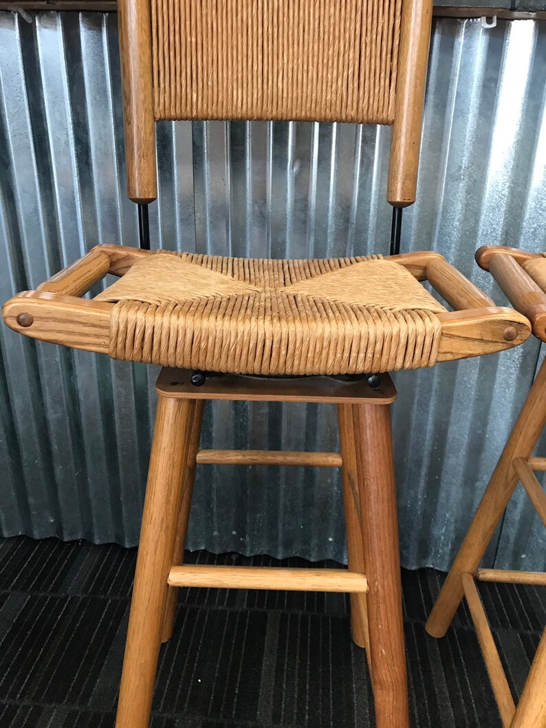 May include: A wooden bar stool with a woven cane seat and back. The stool has a simple design with four legs and a footrest.