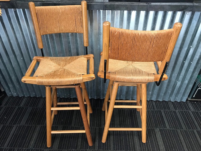 May include: Two wooden bar stools with woven cane seats and backs. The stools have a natural wood finish and black metal accents.