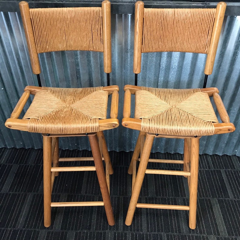 May include: Two wooden bar stools with woven cane seats and backs. The stools have a simple, rustic design and are made of natural wood.