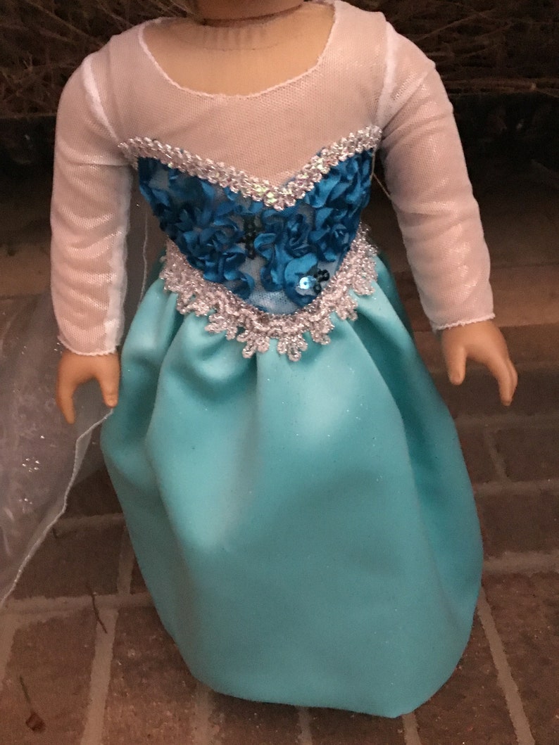 May include: A turquoise blue satin dress with a white mesh overlay and a silver and blue beaded bodice. The dress is designed for a doll.