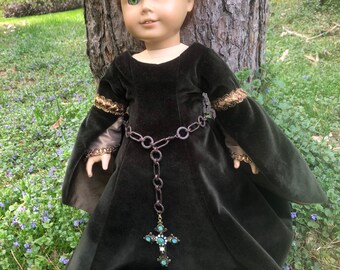 May include: A doll wearing a dark green velvet dress with gold trim and a jeweled chain belt. The doll has brown hair and green eyes and is wearing a jeweled headband.