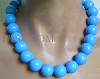 May include: A light blue beaded necklace with large, round beads. The necklace is on a mannequin's neck.