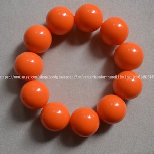 Könnte beinhalten: Ein Armband aus zehn leuchtend orangefarbenen runden Perlen. Die Perlen sind alle gleich groß und auf einer durchsichtigen Gummikordel aufgefädelt.