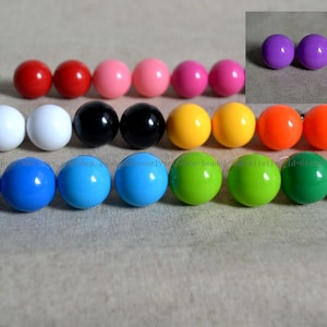 May include: A set of 12 pairs of colourful round earrings. The earrings are made of plastic and come in a variety of colours, including red, pink, yellow, orange, green, blue, black, and white.