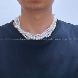 Könnte beinhalten: Eine weiße Perlenkette mit mehreren Strängen. Die Kette wird von einer Person mit einem schwarzen Shirt getragen.