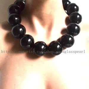 Puede incluir: Un collar de cuentas de vidrio negro con cuentas grandes y redondas. El collar está en el cuello de un maniquí.