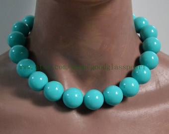 May include: A turquoise blue glass bead necklace with large round beads. The necklace is on a mannequin's neck.