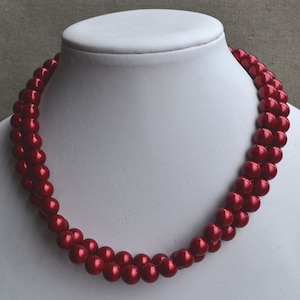 Könnte beinhalten: Eine zweireihige Halskette aus tief roten Kunstperlen. Die Halskette wird auf einer weißen Mannequin-Büste präsentiert.