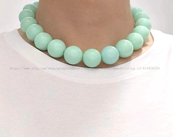 May include: A light green glass bead necklace with large round beads. The necklace is on a white background.