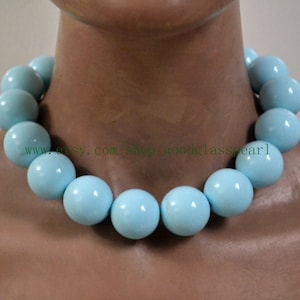 Puede incluir: Un collar de cuentas de vidrio azul claro con cuentas grandes y redondas. El collar está en el cuello de un maniquí.