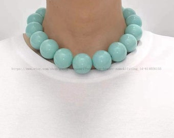 May include: A light blue beaded necklace with large, round beads. The necklace is being worn by a person, but their face is not visible.