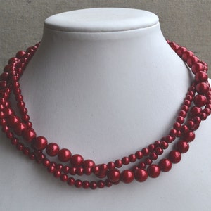 Op de afbeelding: Een meerrijige ketting gemaakt van donkerrode nepparels. De ketting is gelaagd en heeft een klassieke, elegante uitstraling.