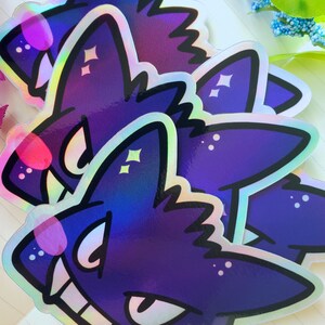 May include: Three iridescent purple and black stickers of a cartoon wolf with a toothy grin and sparkling eyes.