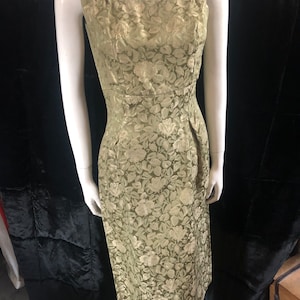 Może przedstawiać: Zielona sukienka bez rękawów z kwiatowym wzorem. Sukienka ma dopasowany gorset i lekko rozkloszowaną spódnicę.