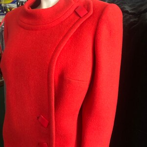 K&ouml;nnte beinhalten: Eine rote Wolljacke mit Stehkragen und diagonalem Verschluss. Die Jacke hat drei rote Kn&ouml;pfe auf der Vorderseite.