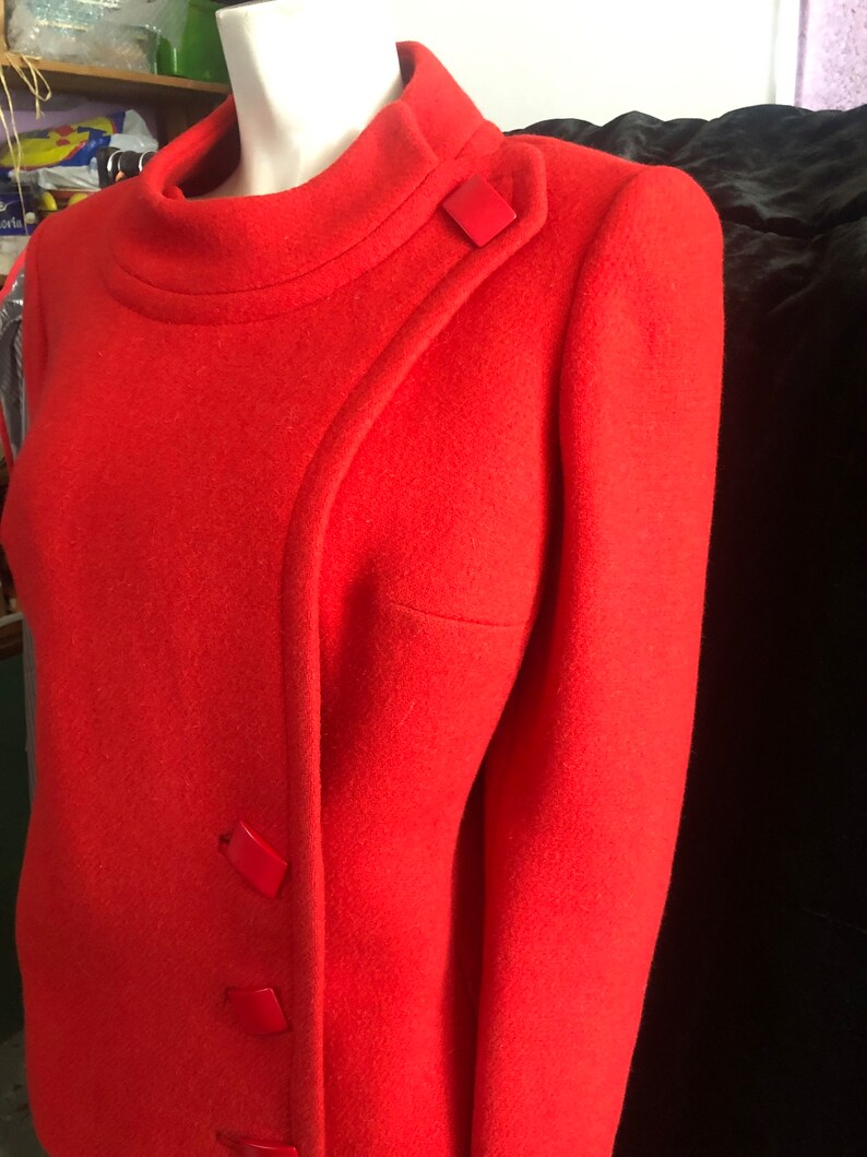 K&ouml;nnte beinhalten: Eine rote Wolljacke mit Stehkragen und diagonalem Verschluss. Die Jacke hat drei rote Kn&ouml;pfe auf der Vorderseite.