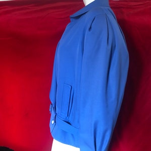 May include: A blue jacket with a belted waist and a collar. The jacket has a slightly puffed sleeve and a single button closure.