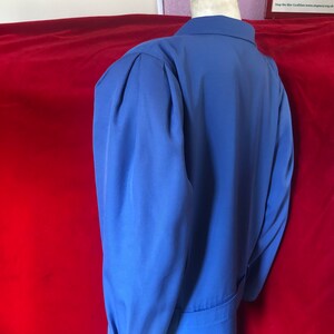 May include: A blue blazer with a long sleeve and a button-up collar. The blazer has a single button closure and a belt.