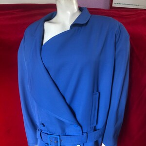 May include: A blue blazer with a single button closure, a belt, and a single pocket on the right side. The blazer has a collar and long sleeves.