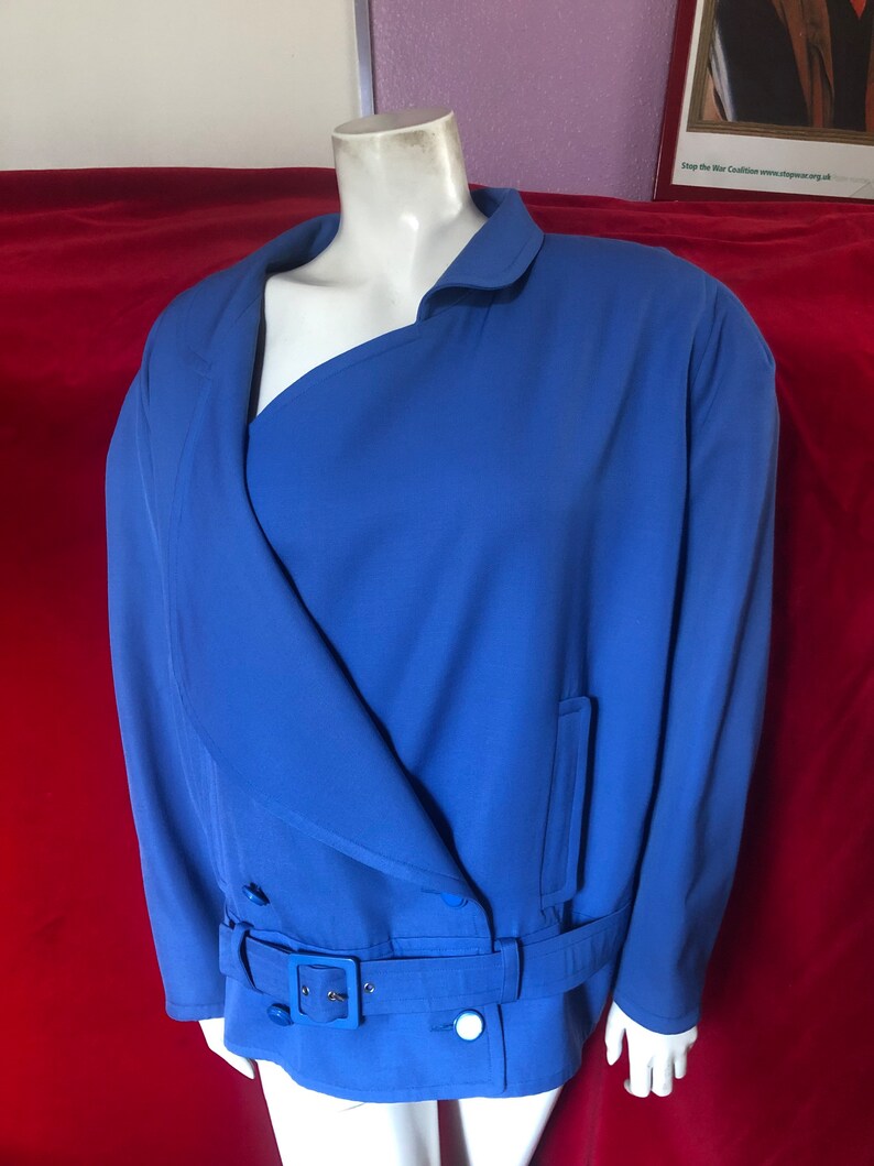 May include: A blue blazer with a single button closure, a belt, and a single pocket on the right side. The blazer has a collar and long sleeves.