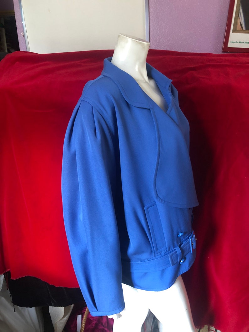 May include: A blue blazer with a long sleeve, a collar, and a belt with a buckle. The blazer is on a white mannequin.