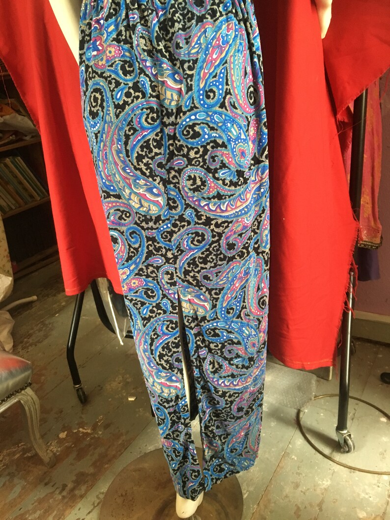May include: A long black skirt with a paisley pattern in shades of blue, pink, and white. The skirt has a center slit and is made of a soft, flowing fabric.
