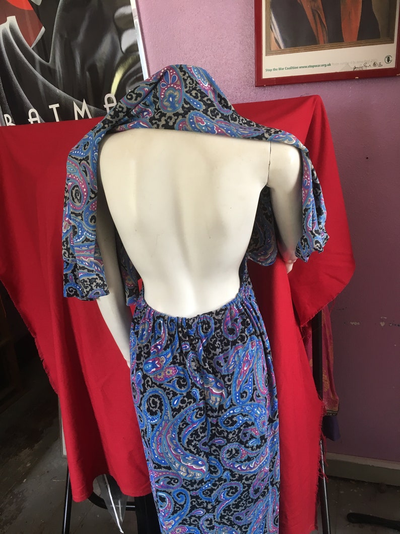 May include: A black and blue paisley print maxi dress with a halter neckline and a low back. The dress is on a mannequin.