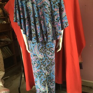 May include: A long, blue and black paisley print dress with a cape-like top. The dress has a slit up the back and is fitted through the bodice.