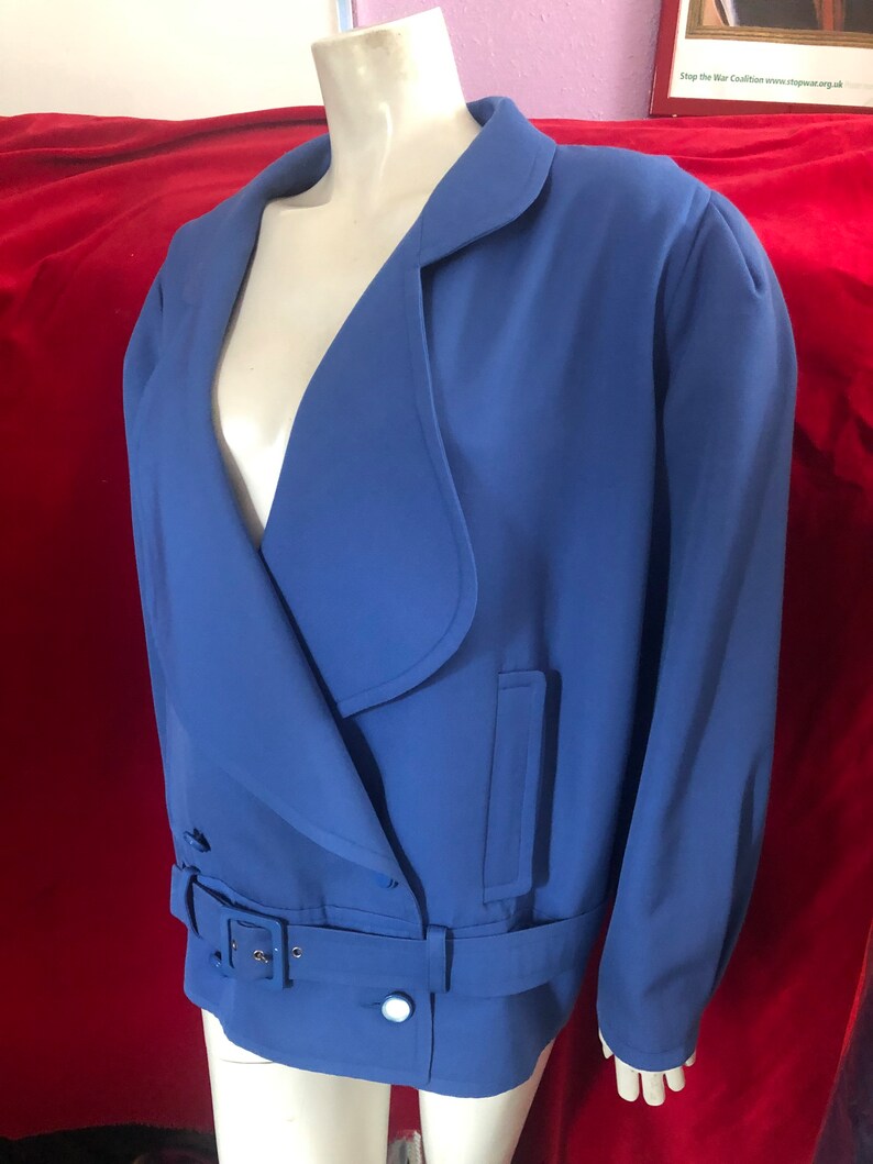 May include: A blue blazer with a long, pointed collar and a belt. The blazer has a single button closure and two pockets.
